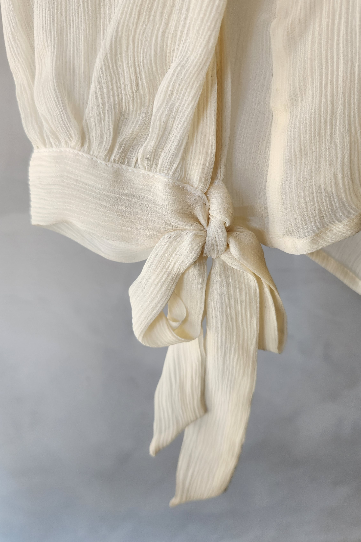 Detalle lazo delantero blusa Luisa Becaria marfil de seda plisada mostrando textura suave y acabado artesanal italiano