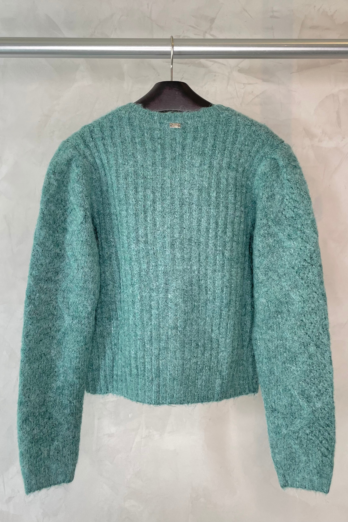 Vista trasera del cardigan Pho Firenze en color verde bosque colgado en percha, mostrando el acabado y detalles del tejido de lana merino