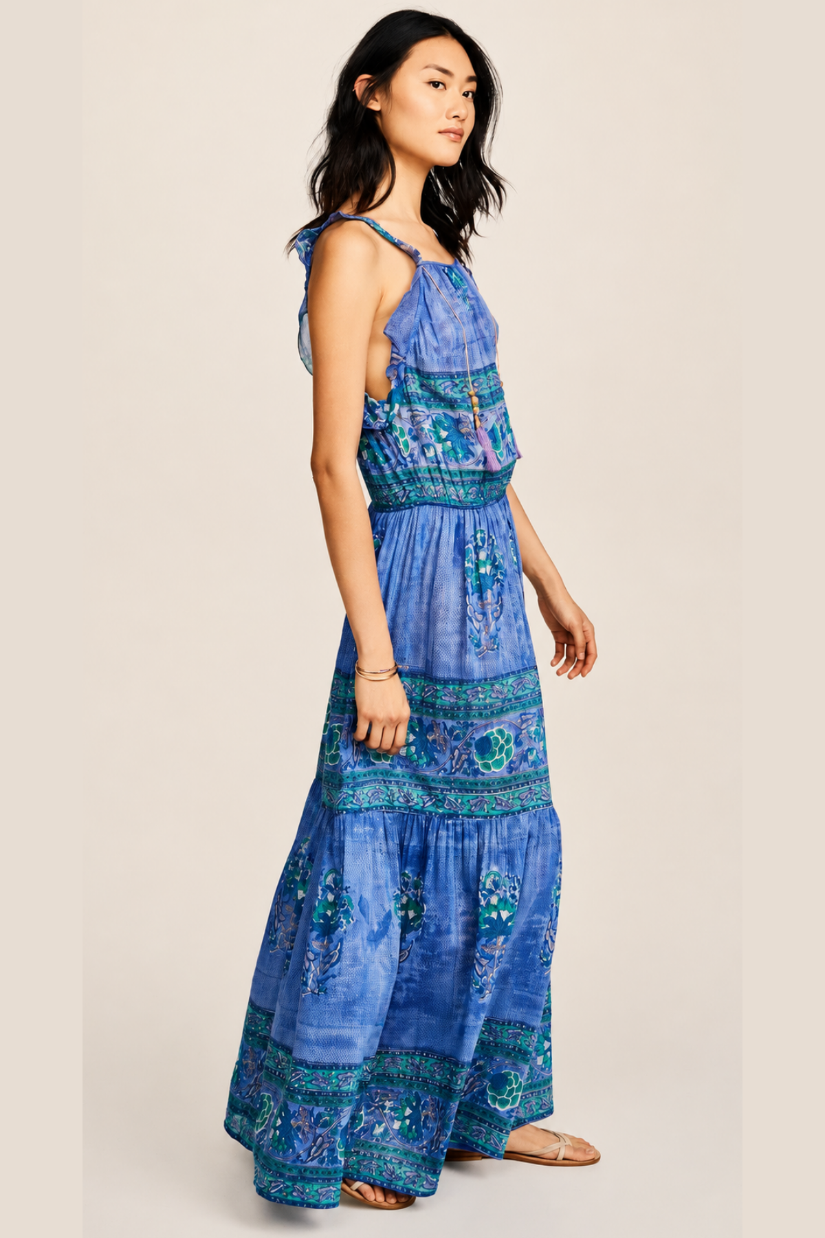Modelo posando de perfil sobre fondo blanco con vestido largo Bell azul, mostrando volante en sisa, cintura elástica y silueta fluida
