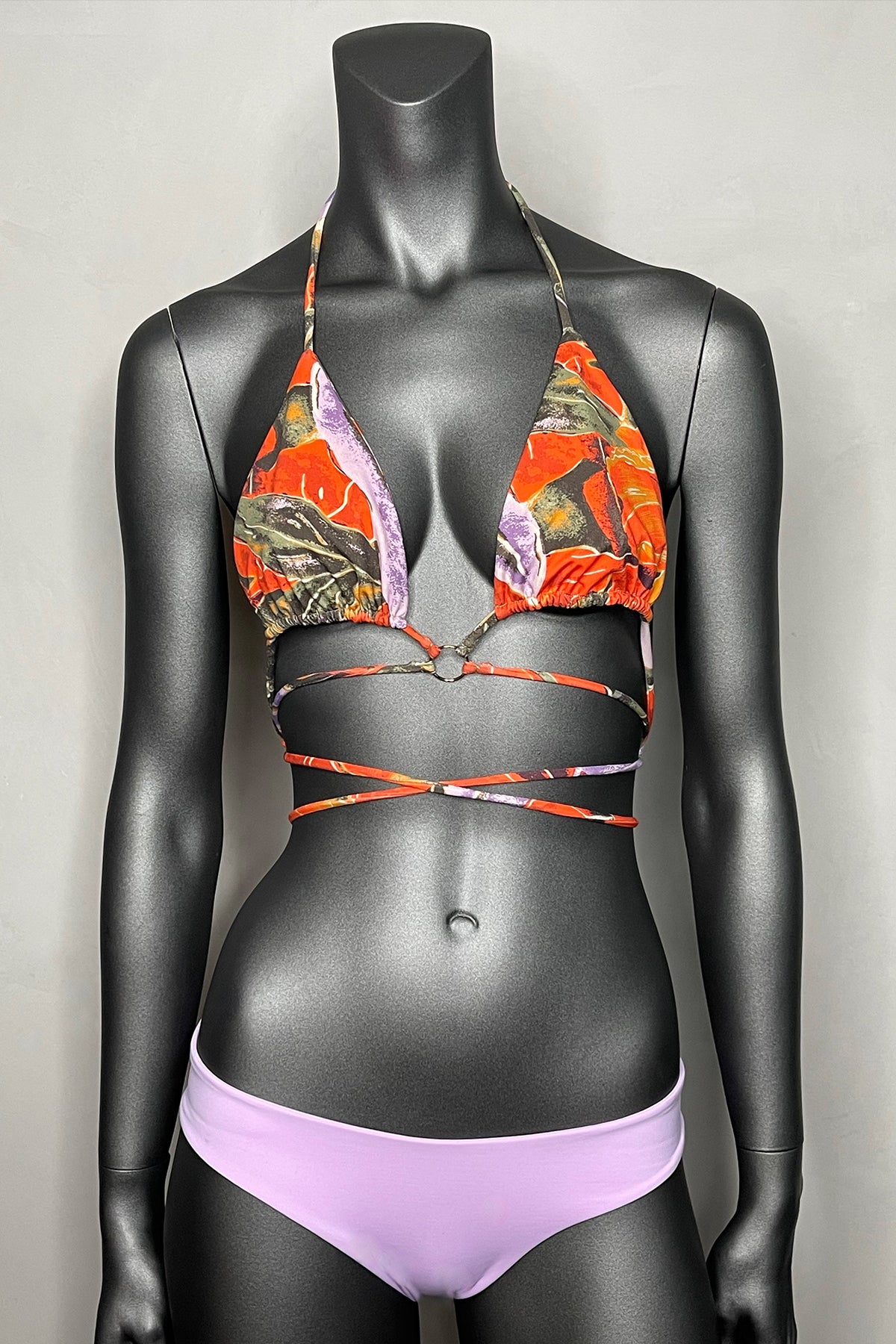 Bikini Indah Tamika expuesto en maniquí, top triángulo con estampado tropical y braguita lisa lila de lycra elástica