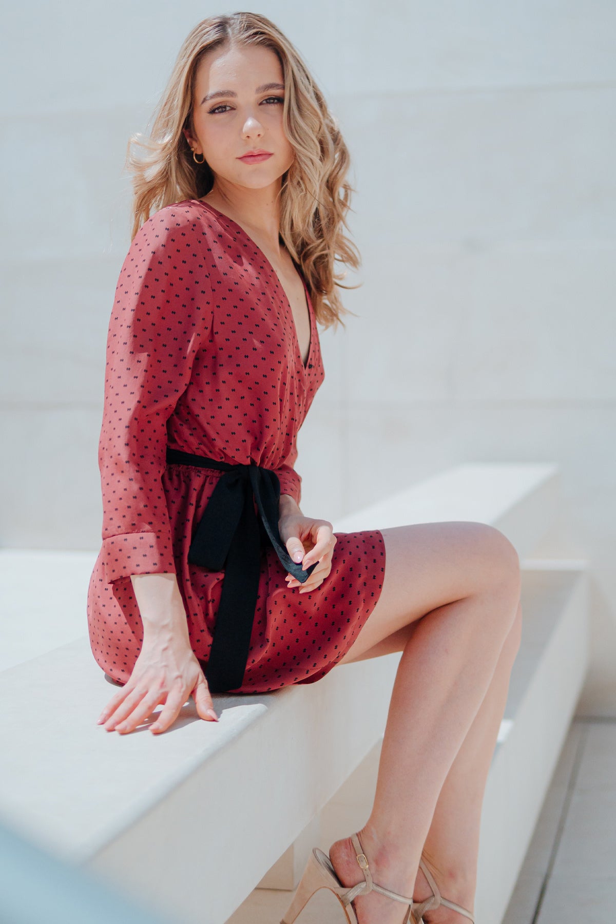 Modelo sentada con vestido corto Eskell Eva en rust, escote en V y estampado minimalista, capturando una pose sofisticada sobre fondo neutro