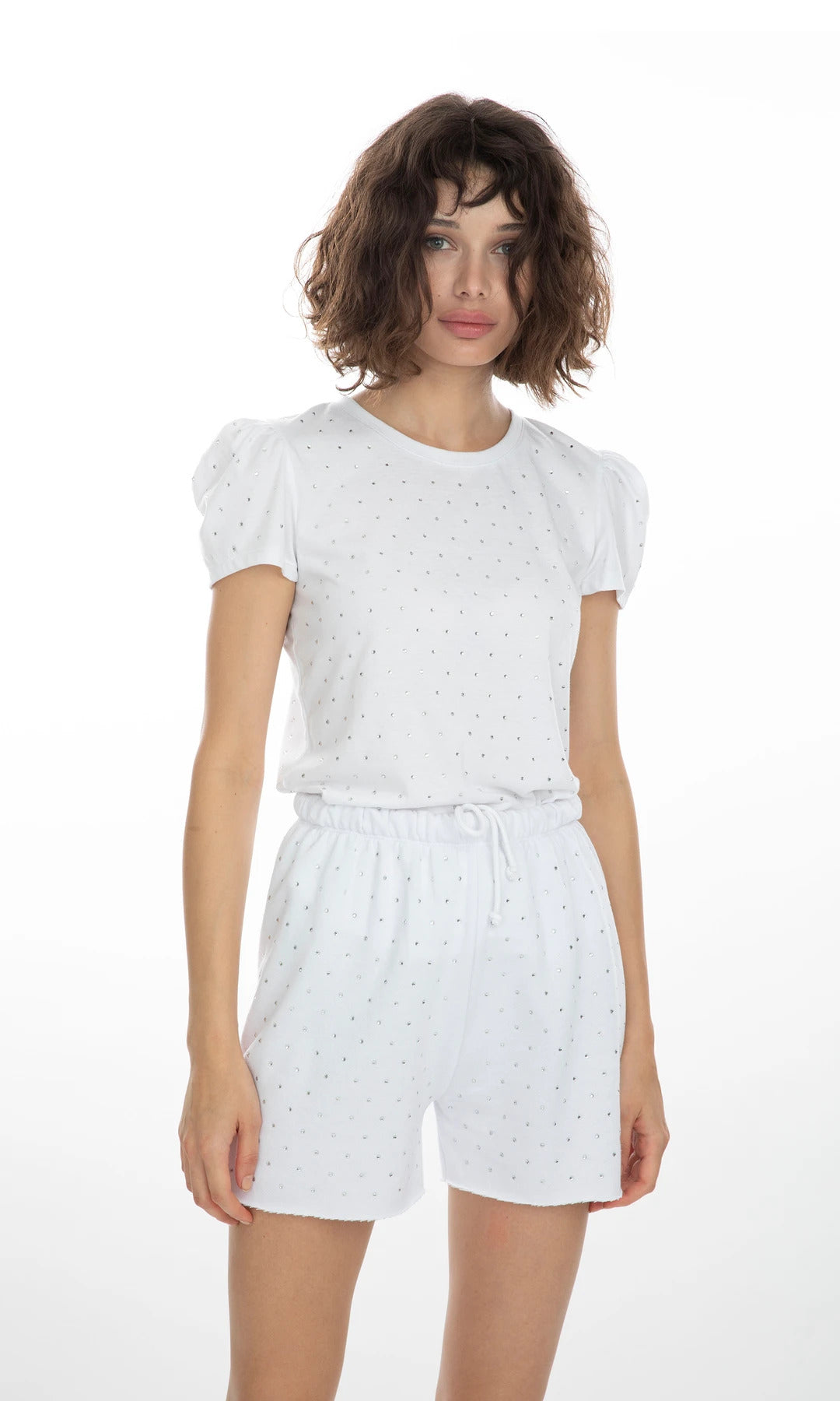 Modelo posando de frente con los shorts blancos Aria Crystal, look veraniego con cintura alta y detalle brillante elegante