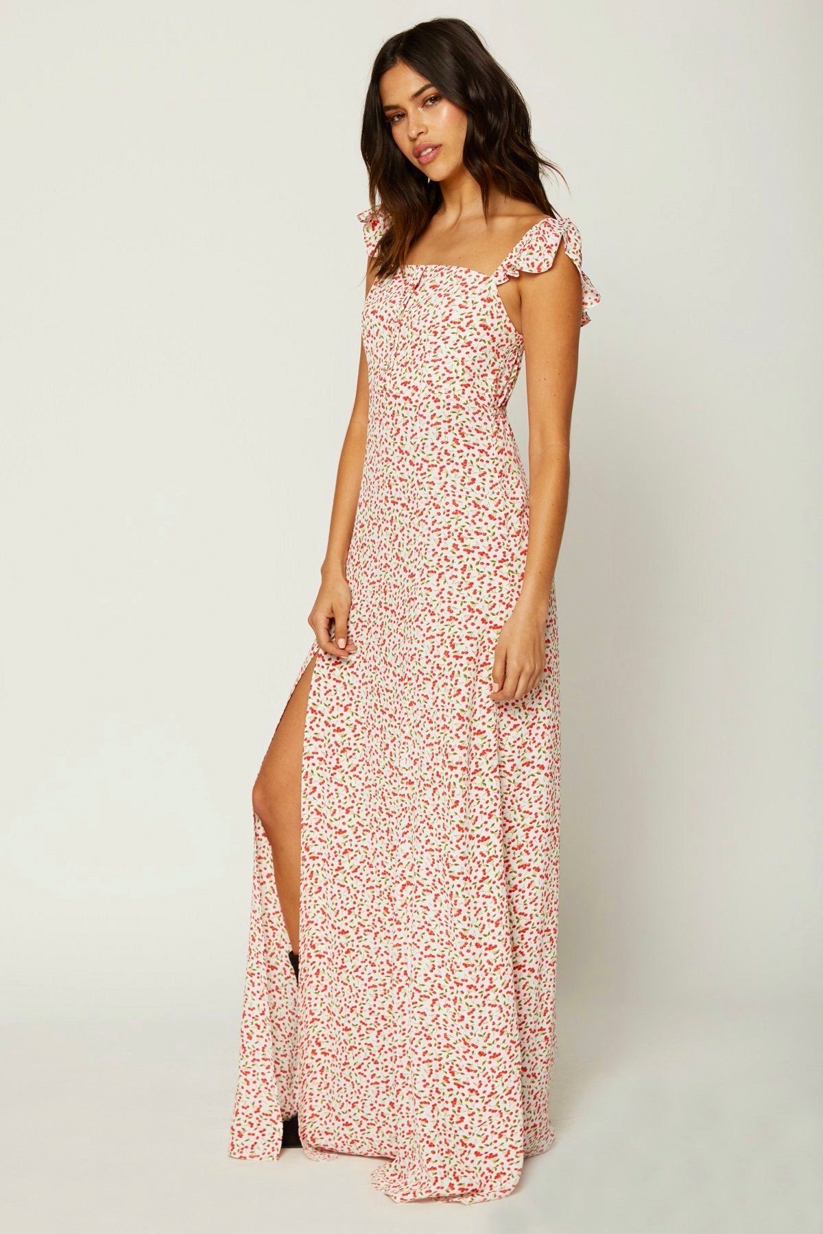 Modelo con vestido largo Flynn Skye Bardot color Sweet Cherry Pie, tirantes de volantes y abertura lateral sobre fondo blanco
