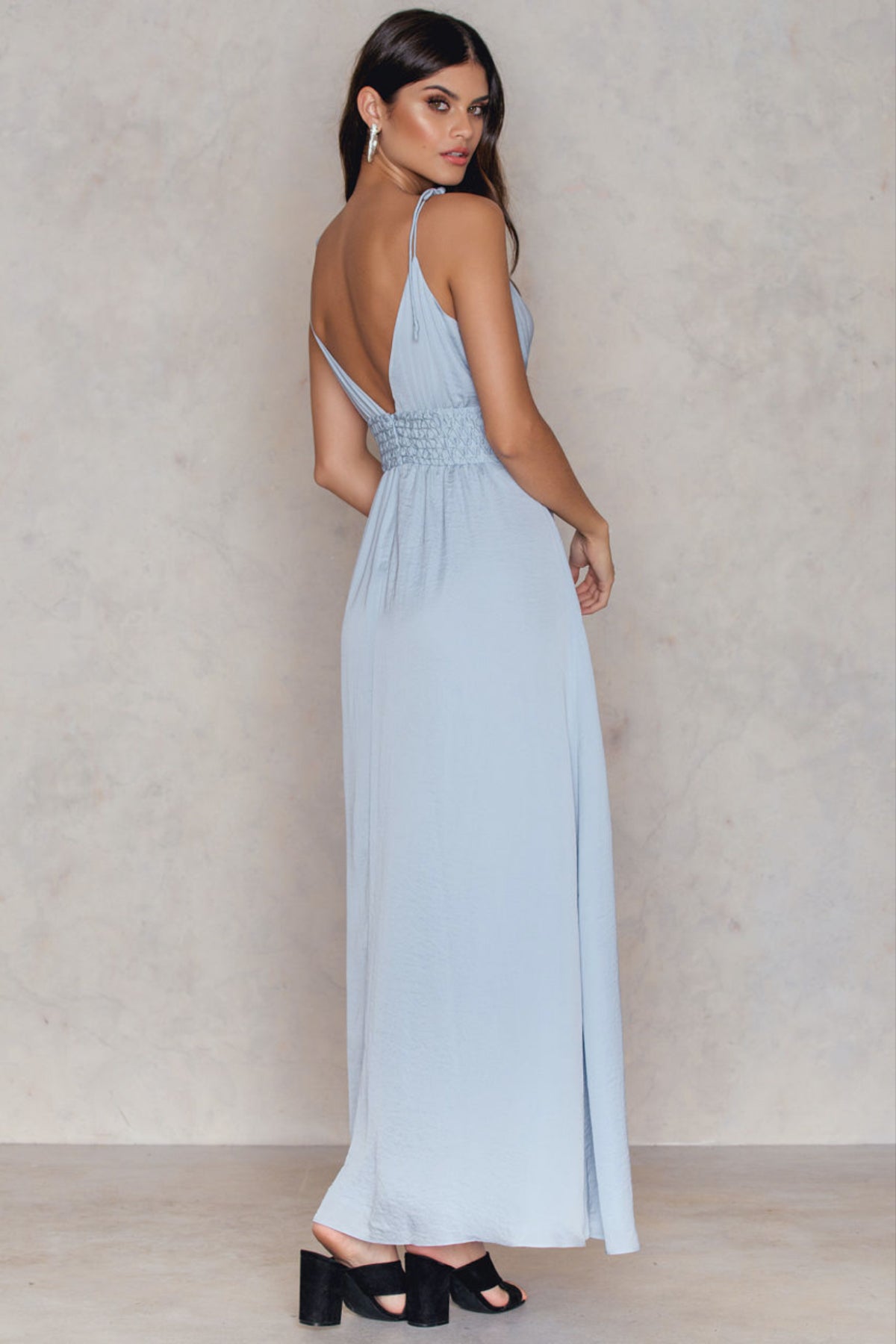 Modelo de espaldas sobre fondo blanco con vestido Blaire baby blue, mostrando tirantes cruzados y caída elegante hasta el suelo