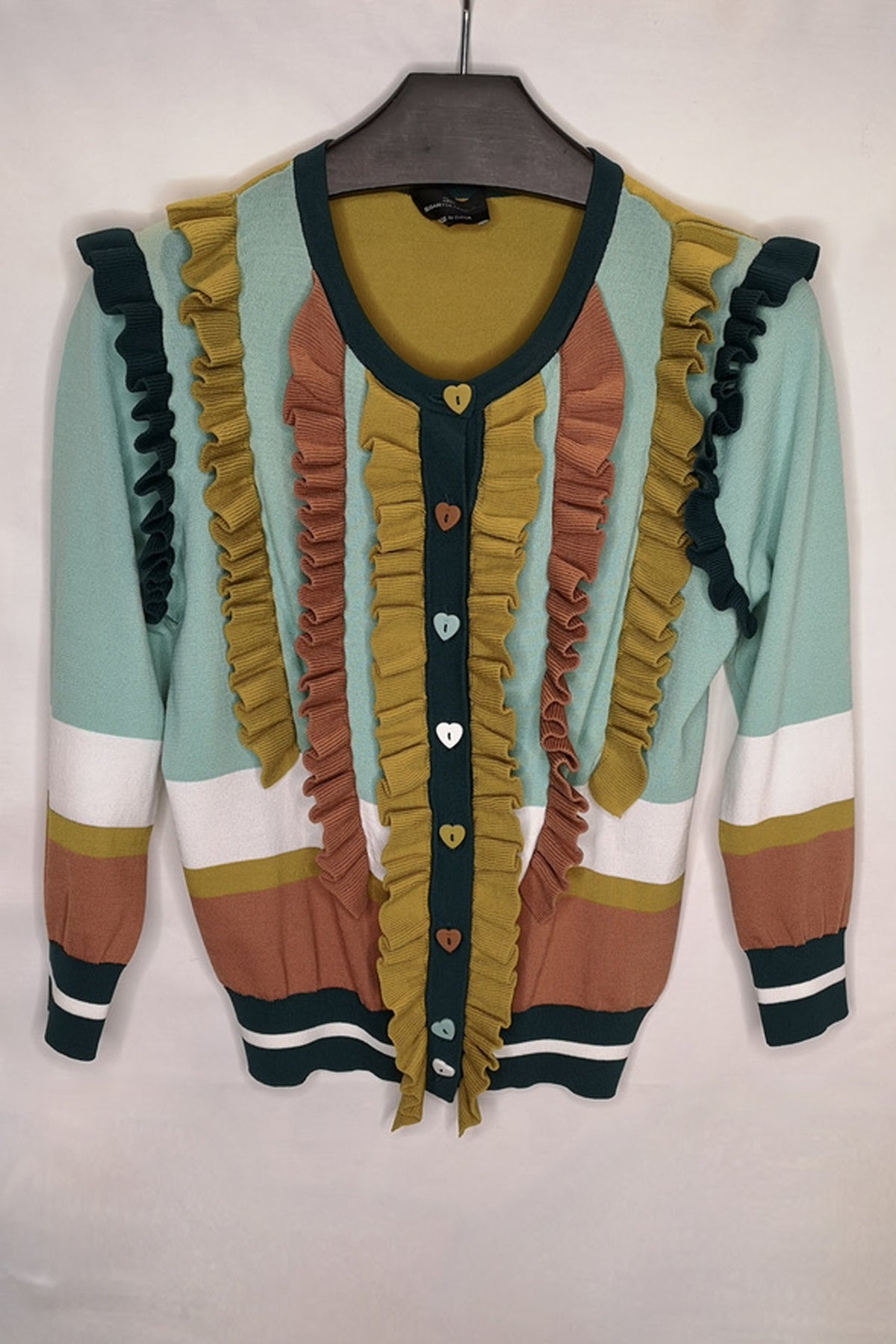 Prenda ligera abierta con volantes suaves y detalle decorativo de corazón, ideal para combinar con jeans o faldas midi