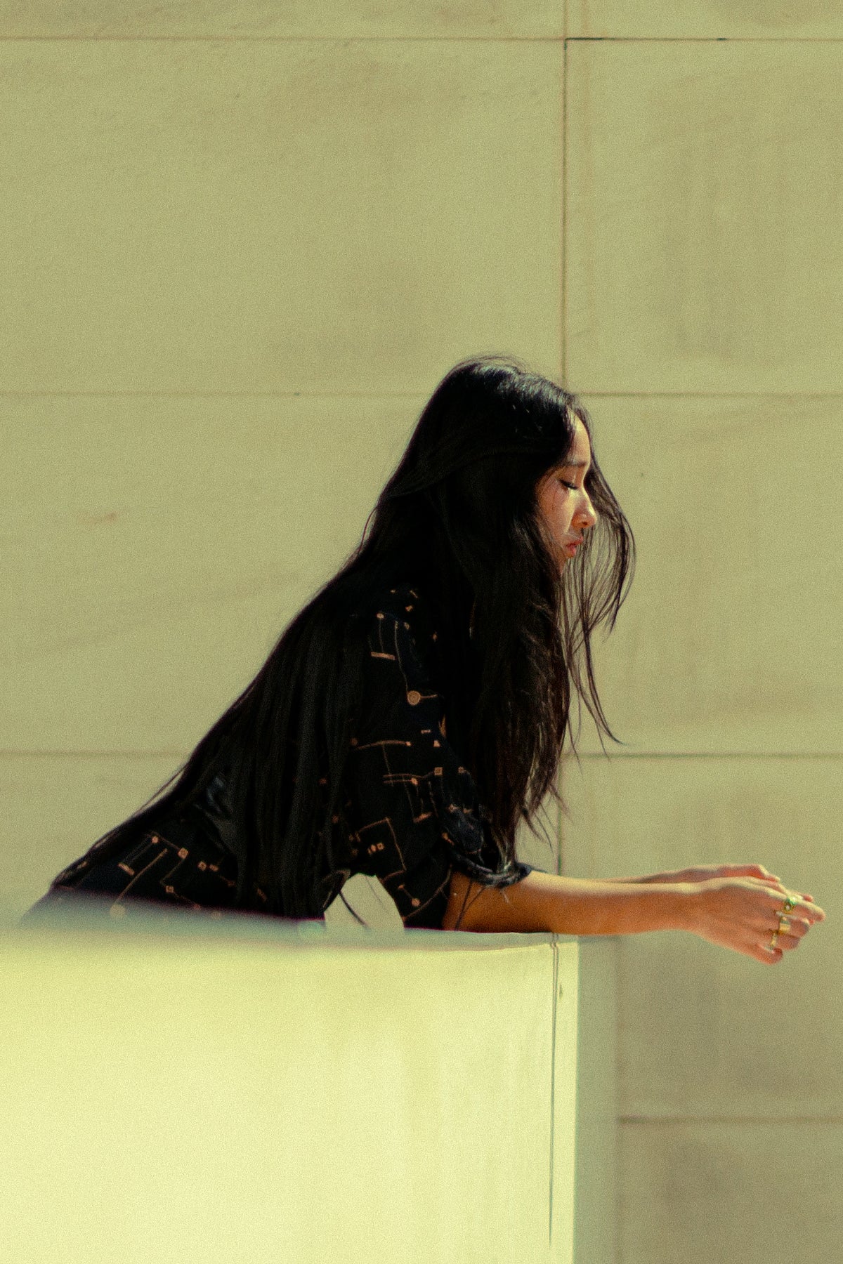 Modelo apoyada en un muro con vestido Eskell Esme negro y estampado dorado, capturando su estilo relajado y elegante sobre fondo neutro