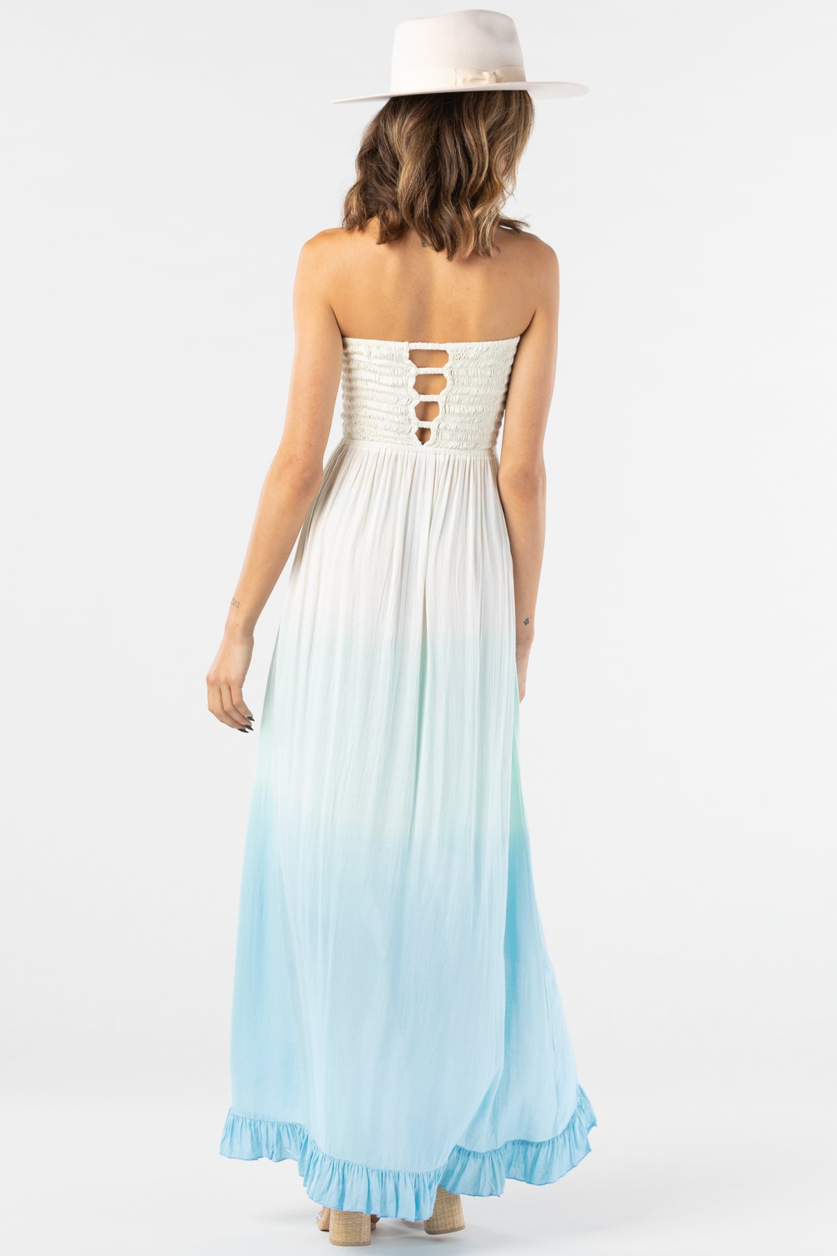 Vista trasera del Flynn maxi dress degradado crema‑teal‑blue en maniquí, con detalle de cut‑out en espalda y caída fluida