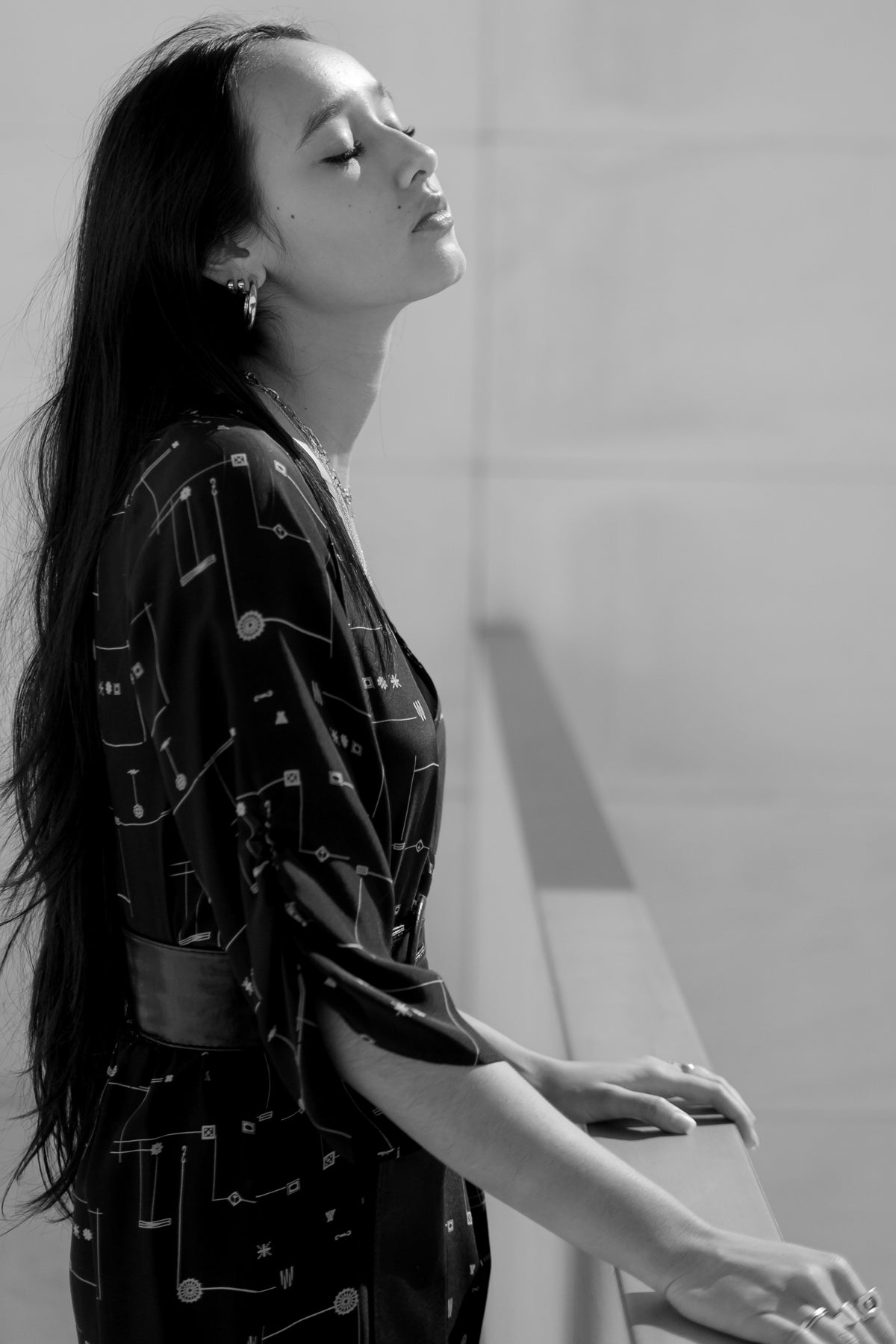 Modelo de pie de perfil con vestido Eskell Esme negro y estampado dorado, mostrando caída fluida y cintura definida