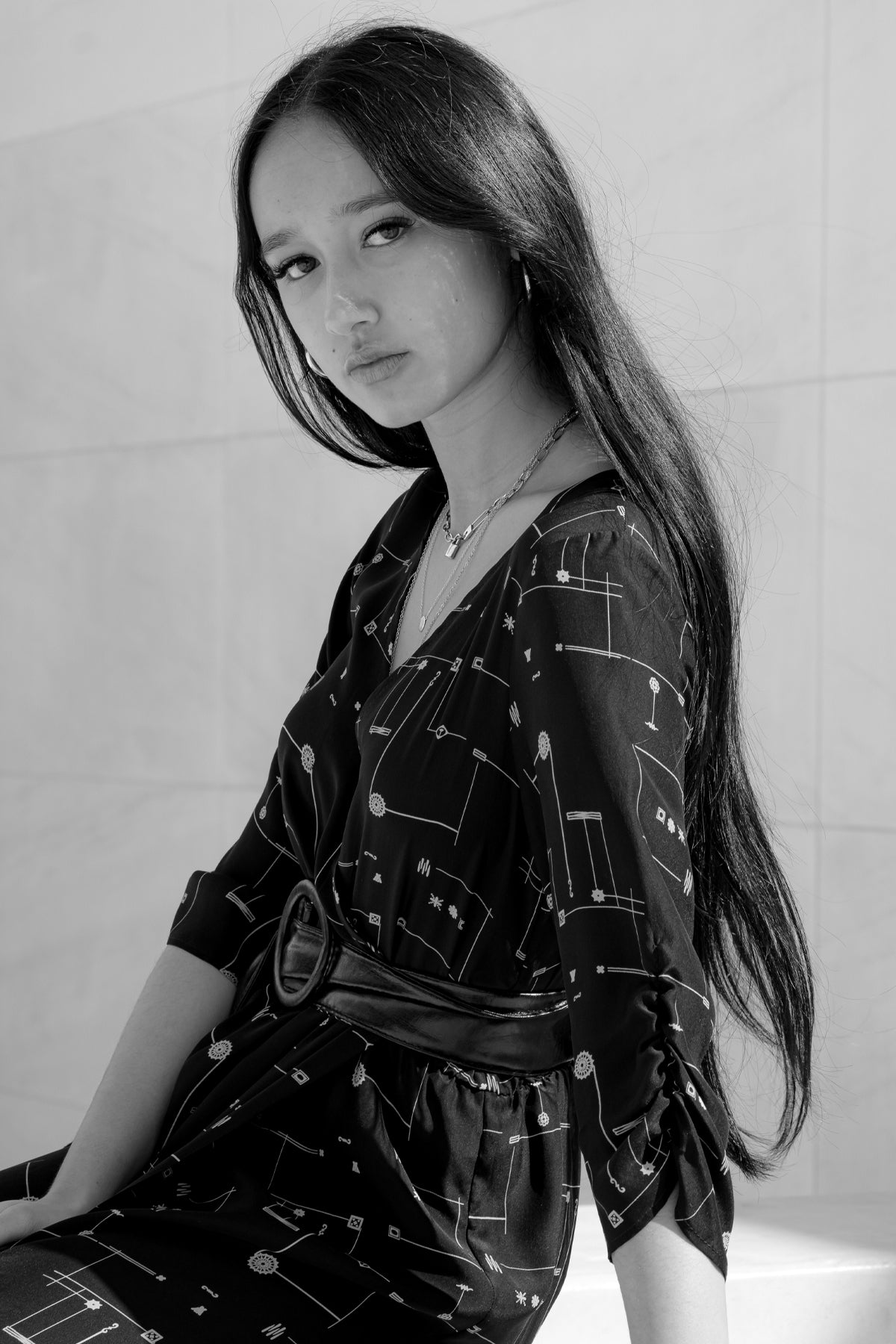 Modelo de perfil con vestido corto Eskell Esme negro con estampado dorado minimalista, mangas ¾ y escote en V sobre fondo neutro