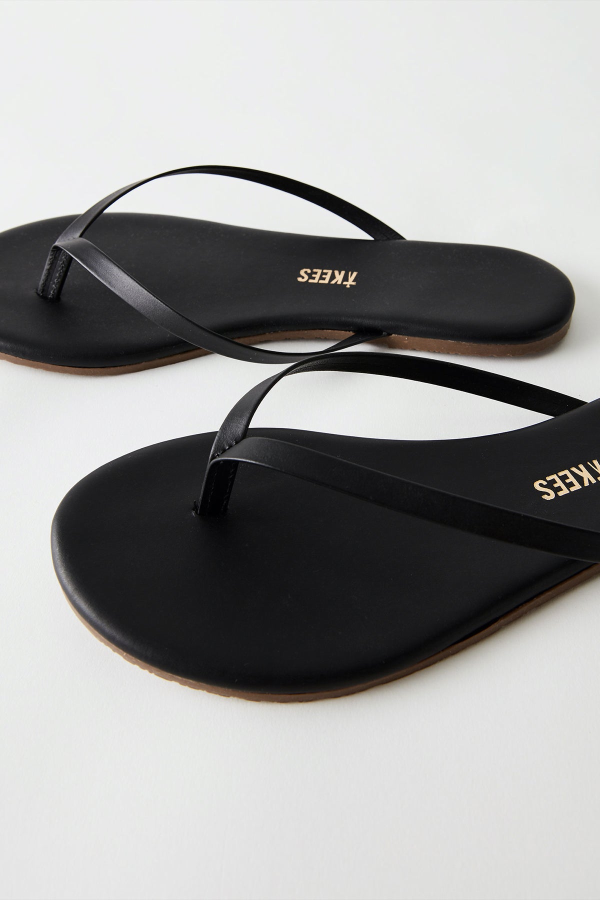 Primer plano de la tira de las Tkees Black Flip Flops en negro, fabricadas con materiales duraderos y resistentes al desgaste