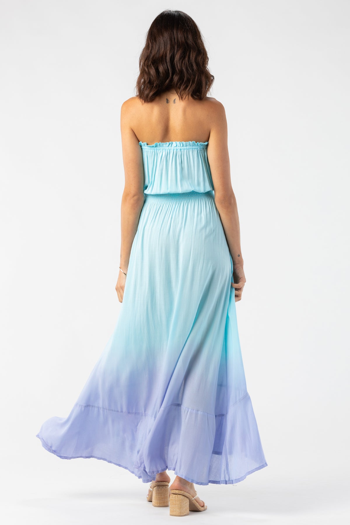 Modelo posando de espaldas con vestido largo Ryden de Tiare Hawaii mostrando el diseño y corte trasero del vestido