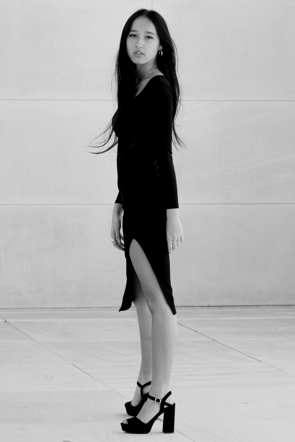 Imagen en blanco y negro de modelo posando lateralmente con vestido Vila negro, resaltando la silueta ajustada