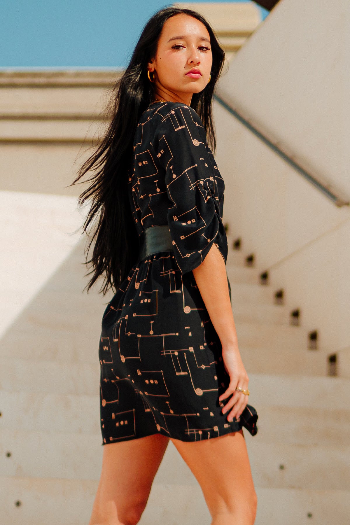 Vista trasera del vestido corto Eskell Esme negro con estampado dorado y cintura elástica, sobre fondo neutro