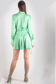Vista trasera de la modelo con vestido corto silk wrap fucsia de Margherita Mazzei mostrando nudo lateral y caída fluida en fondo neutro