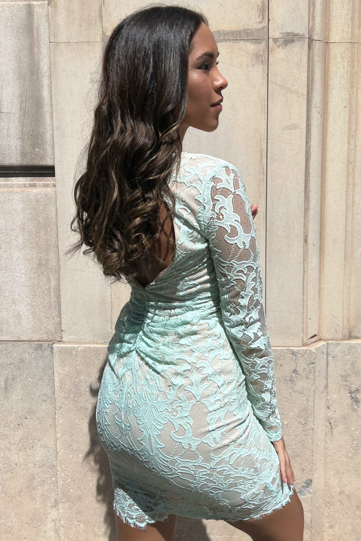 Modelo de espaldas posando con vestido midi de encaje Angel Biba en verde menta sobre fondo neutro, mostrando espalda abierta y caída elegante