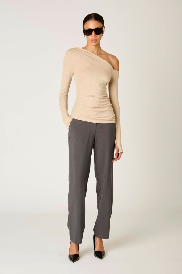 Modelo con top Cleo oatmeal beige de un hombro con manga larga drapeada y pantalones oscuros para look elegante casual