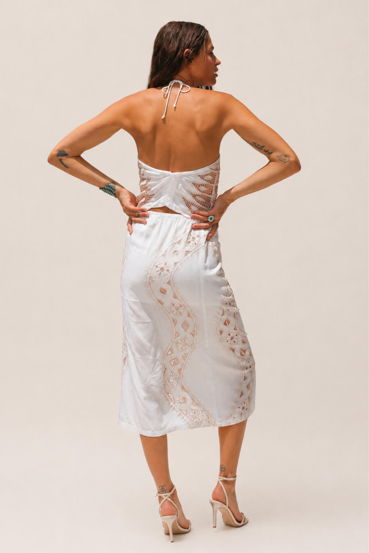 Modelo de pie de espaldas vistiendo un vestido blanco con bordados y detalles transparentes, posando sobre una tela blanca