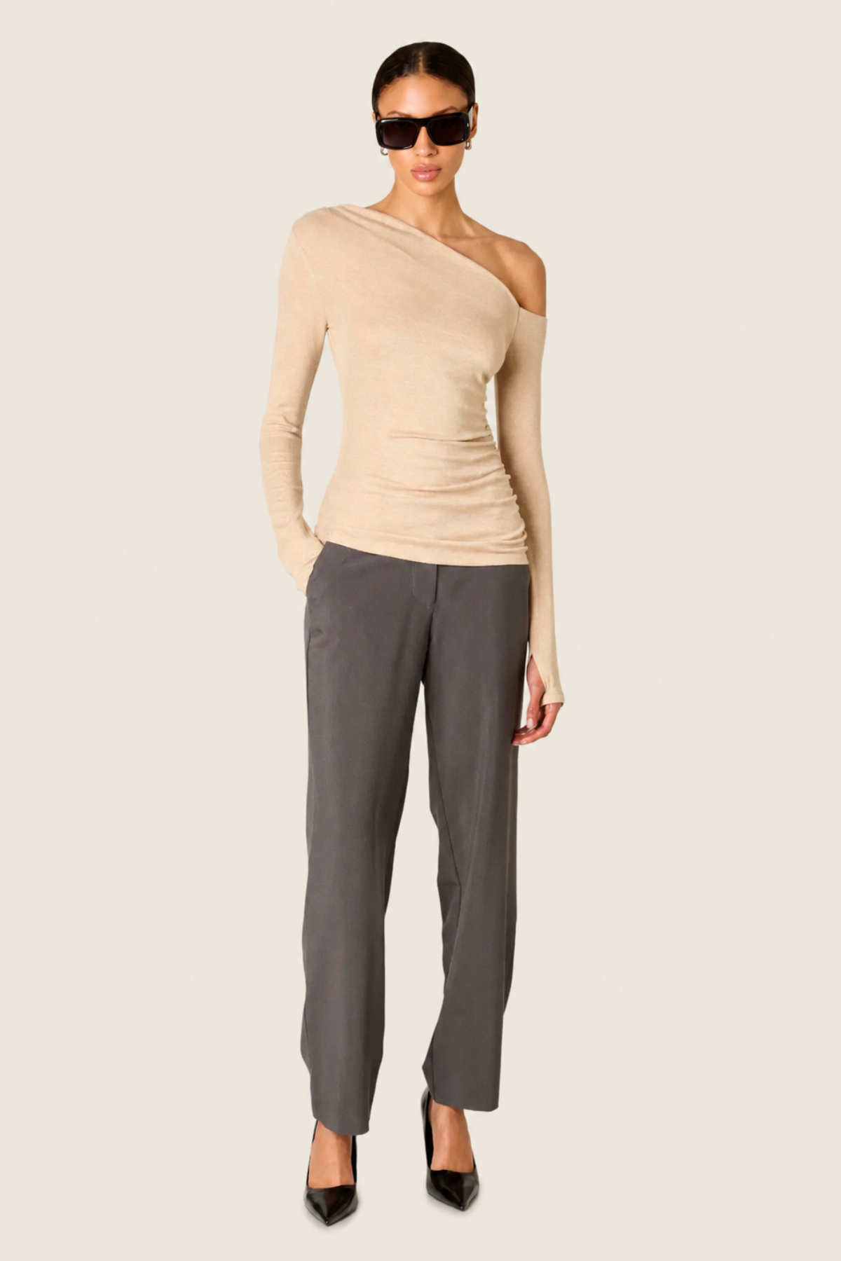Modelo con top Cleo oatmeal beige de un hombro con manga larga drapeada y pantalones oscuros para look elegante casual