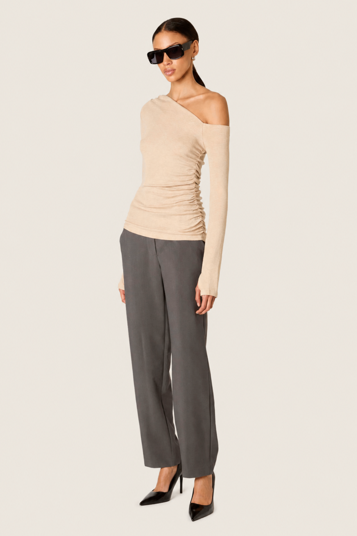 Modelo con top Cleo oatmeal beige de un hombro con manga larga drapeada y pantalones oscuros para look elegante casual