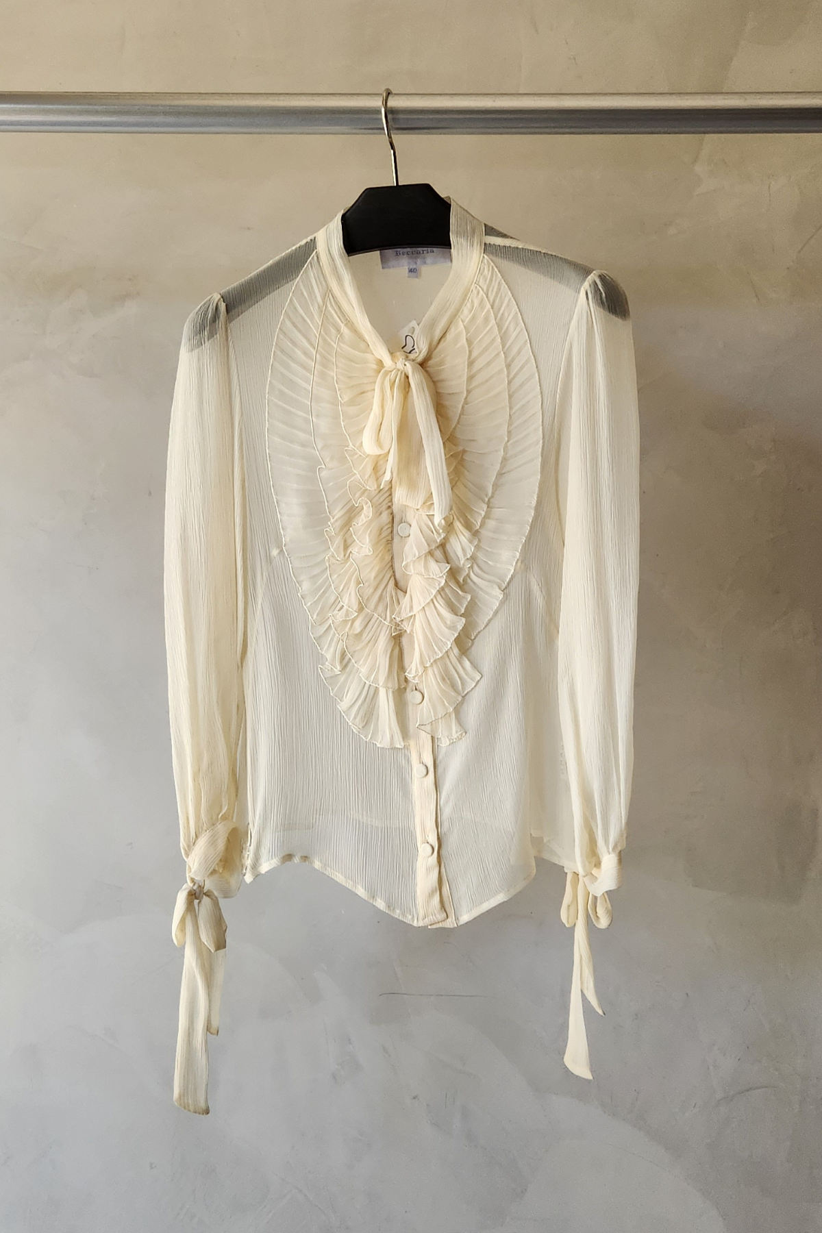 Blusa Luisa Becaria marfil beige de seda con volantes delicados colgada en percha mostrando diseño elegante italiano
