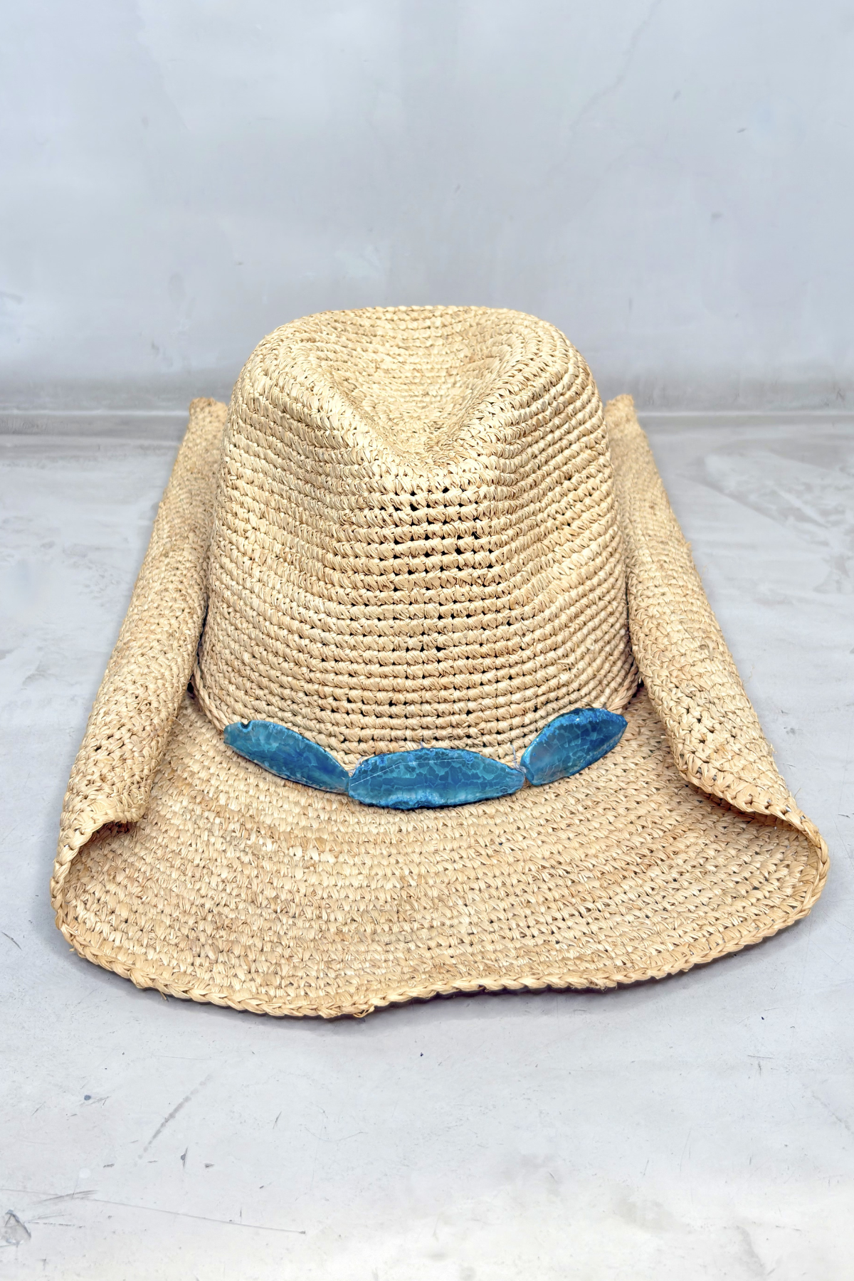 Sombrero de rafia natural con ala ancha y detalle de piedras azules decorativas en la banda