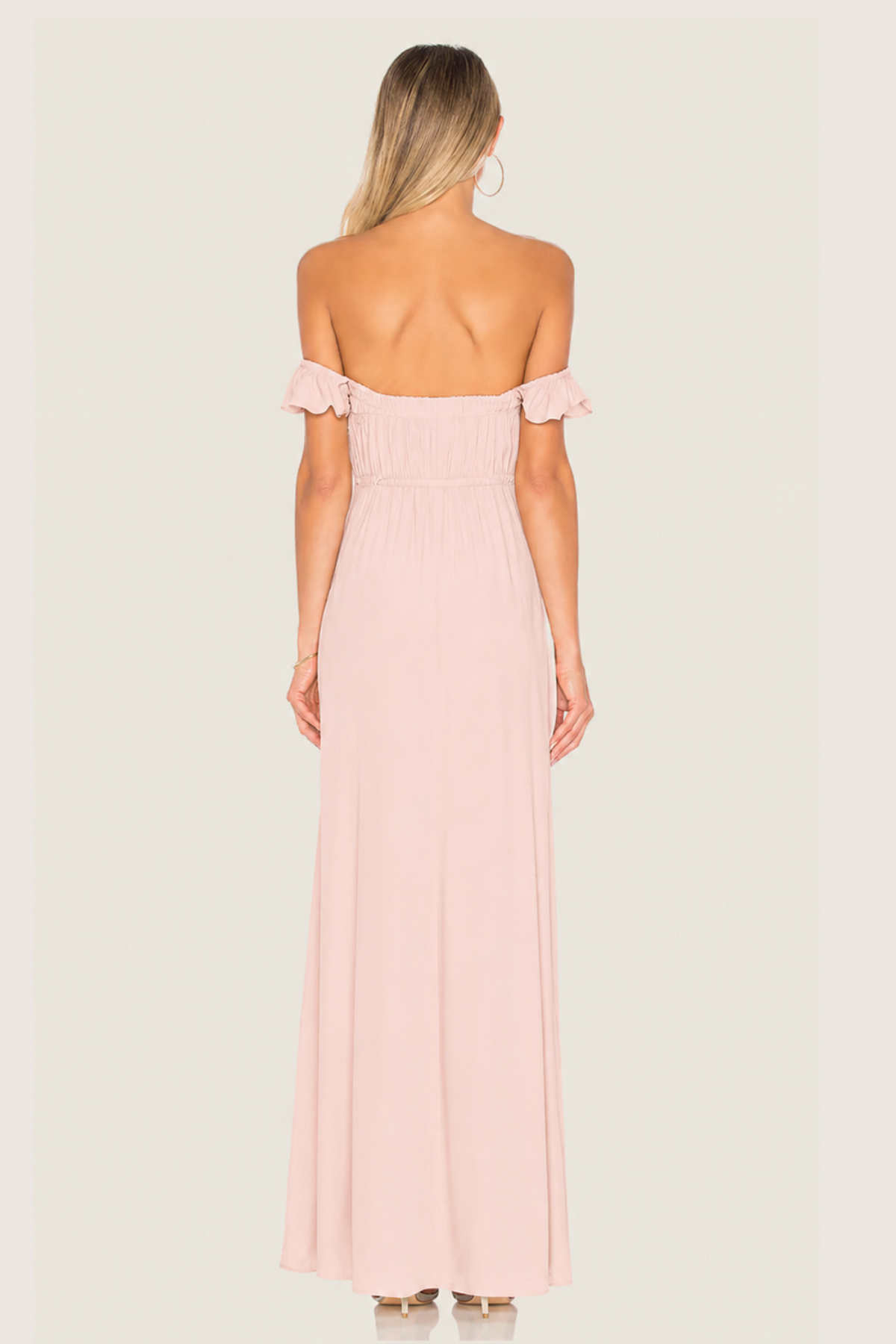 Vista trasera de la modelo con vestido Bardot Sweet Cherry Pie rosa, mostrando espalda descubierta y tirantes de volantes sobre fondo blanco