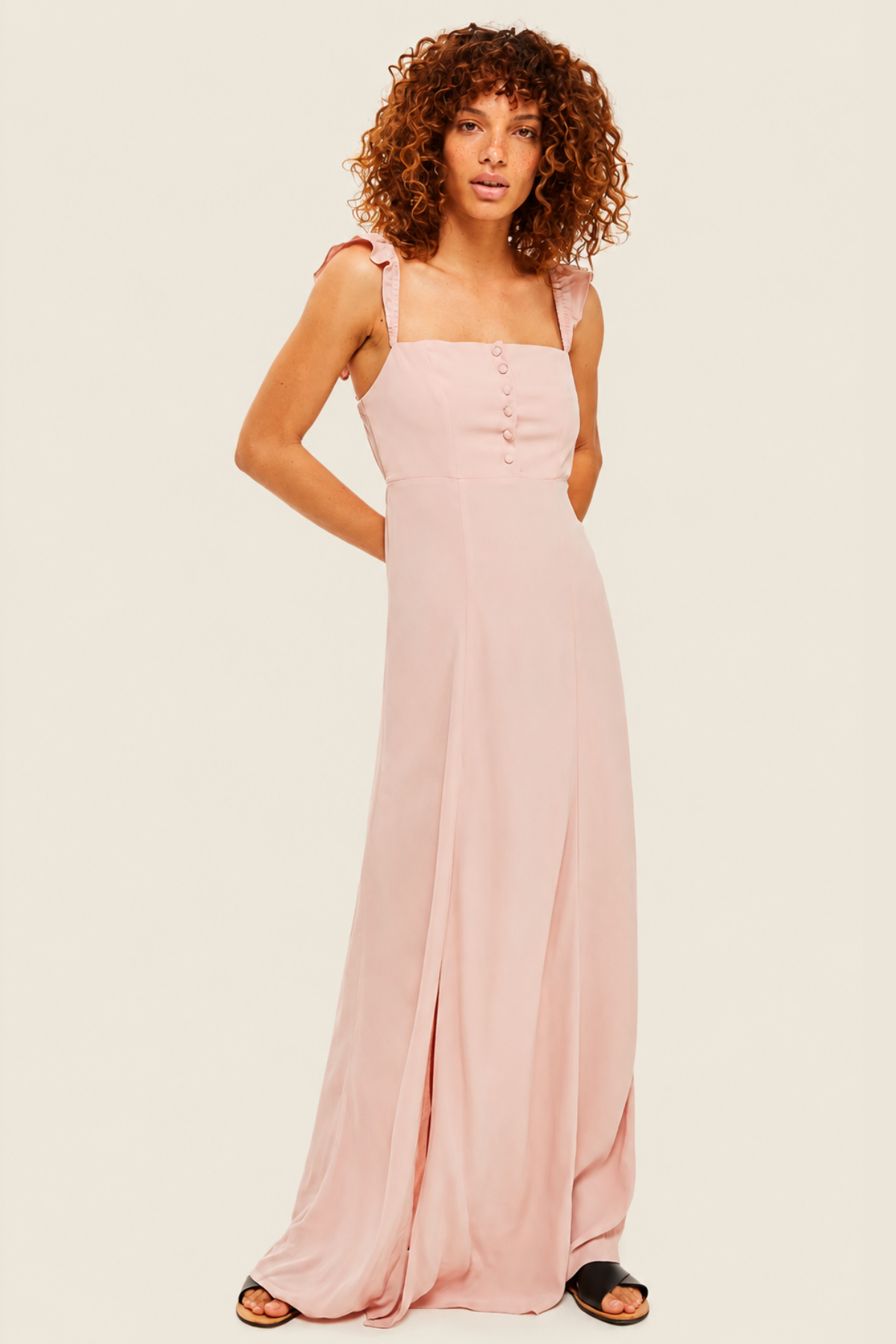 Modelo posando frontalmente con vestido largo Flynn Skye Bardot en rosa claro, tirantes de volantes y abertura lateral
