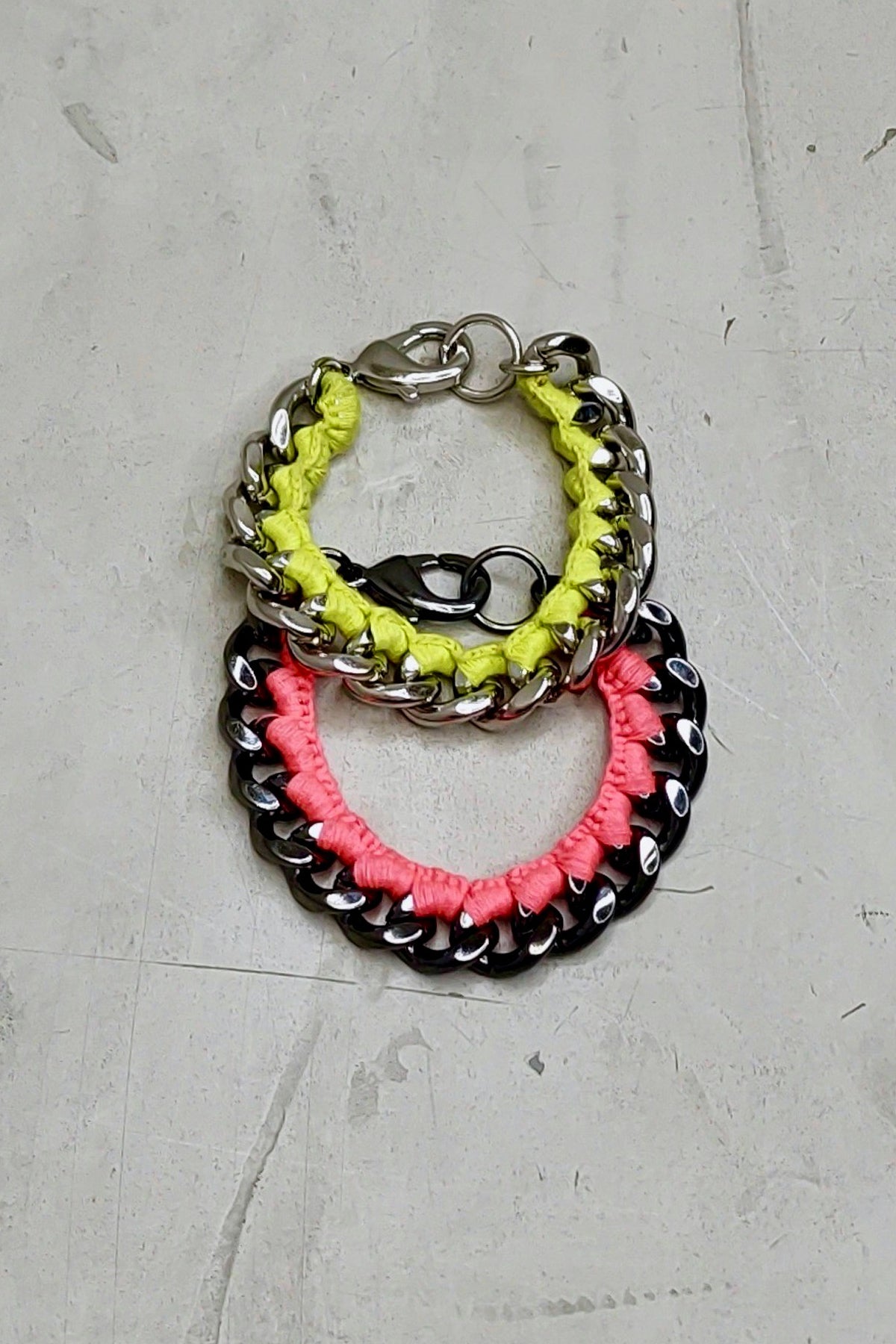Pulseras de cadena en neón rosa y neón amarillo sobre fondo blanco, mostrando sus eslabones grandes y diseño vibrante para un estilo moderno
